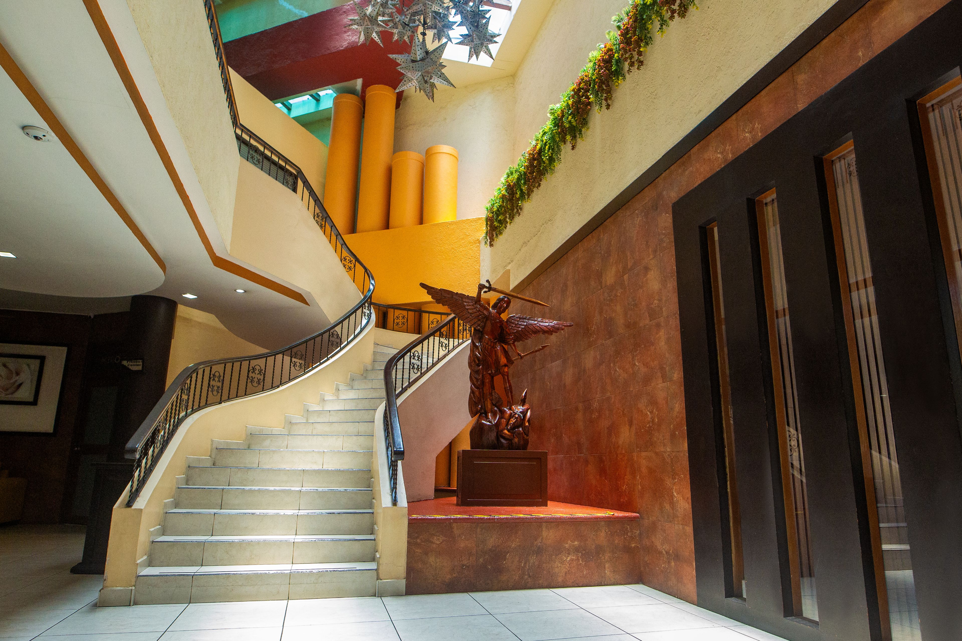 A multi-level interior with a central staircase, a decorative sculpture, and a wall-mounted plant.