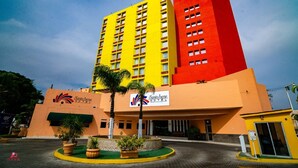 A multi-story hotel with a yellow and red facade, a sign indicating it is the Santa Irene Hotel, and a landscaped entrance area with palm trees.