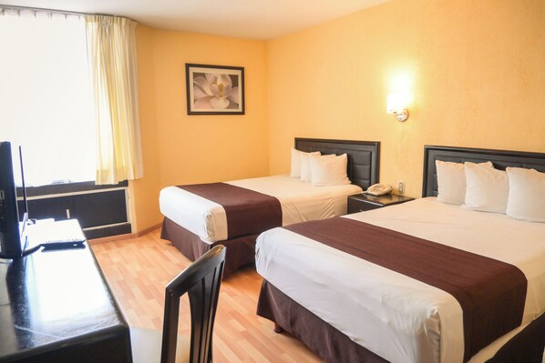 Quarto de hotel com duas camas, uma escrivaninha, uma cadeira, um abajur e um quadro na parede.