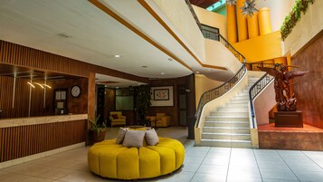 Un vestíbulo de hotel con una escalera, una recepción y una zona de estar amarilla.