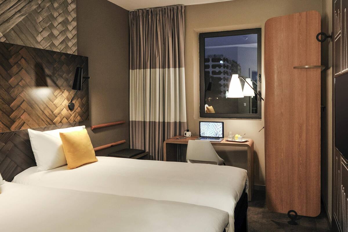 Een hotelkamer met een groot bed, een bureau met een laptop, een stoel en een raam met gordijnen.
