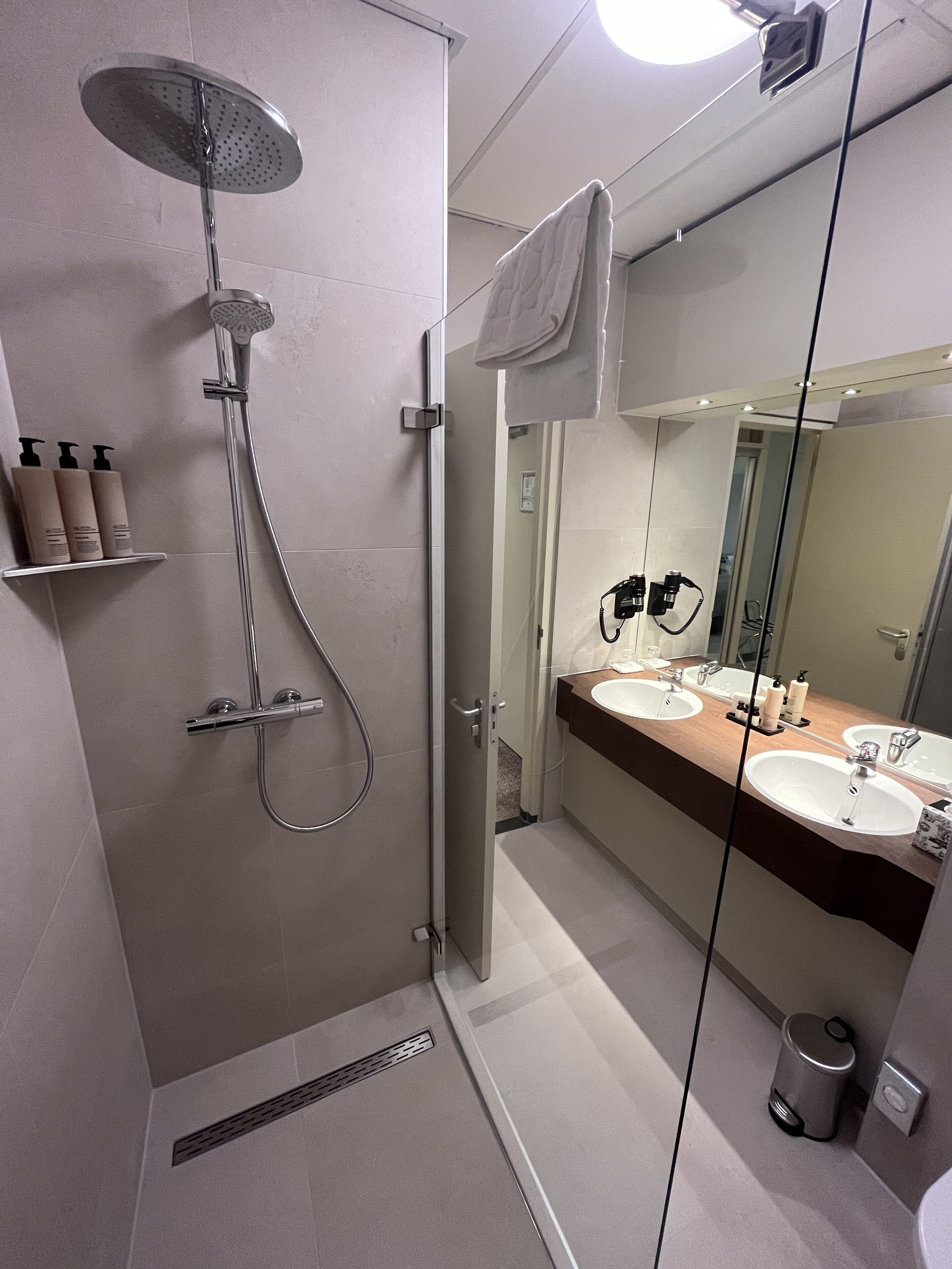 Une salle de bain moderne avec une douche à l’italienne, deux lavabos et un grand miroir.