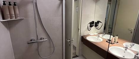 Une salle de bain moderne avec une douche à l’italienne, deux lavabos et un grand miroir.