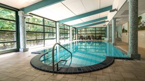 Piscina interior com paredes de vidro transparente, piso ladrilhado e algumas cadeiras de descanso.