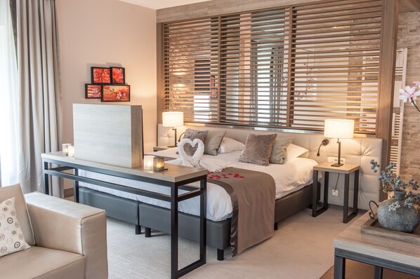Una habitación de hotel moderna con una cama, mesitas de noche, un escritorio, un sofá y un amplio ventanal con persianas.