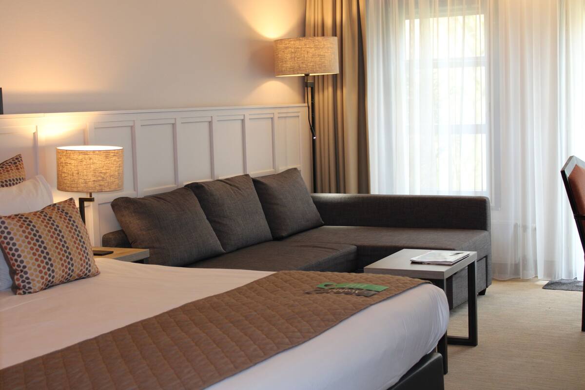Une chambre d’hôtel avec un lit, un canapé, une table et une lampe.