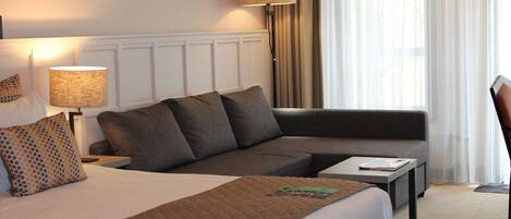 A hotel room with a bed, a sofa, a table, and a lamp.