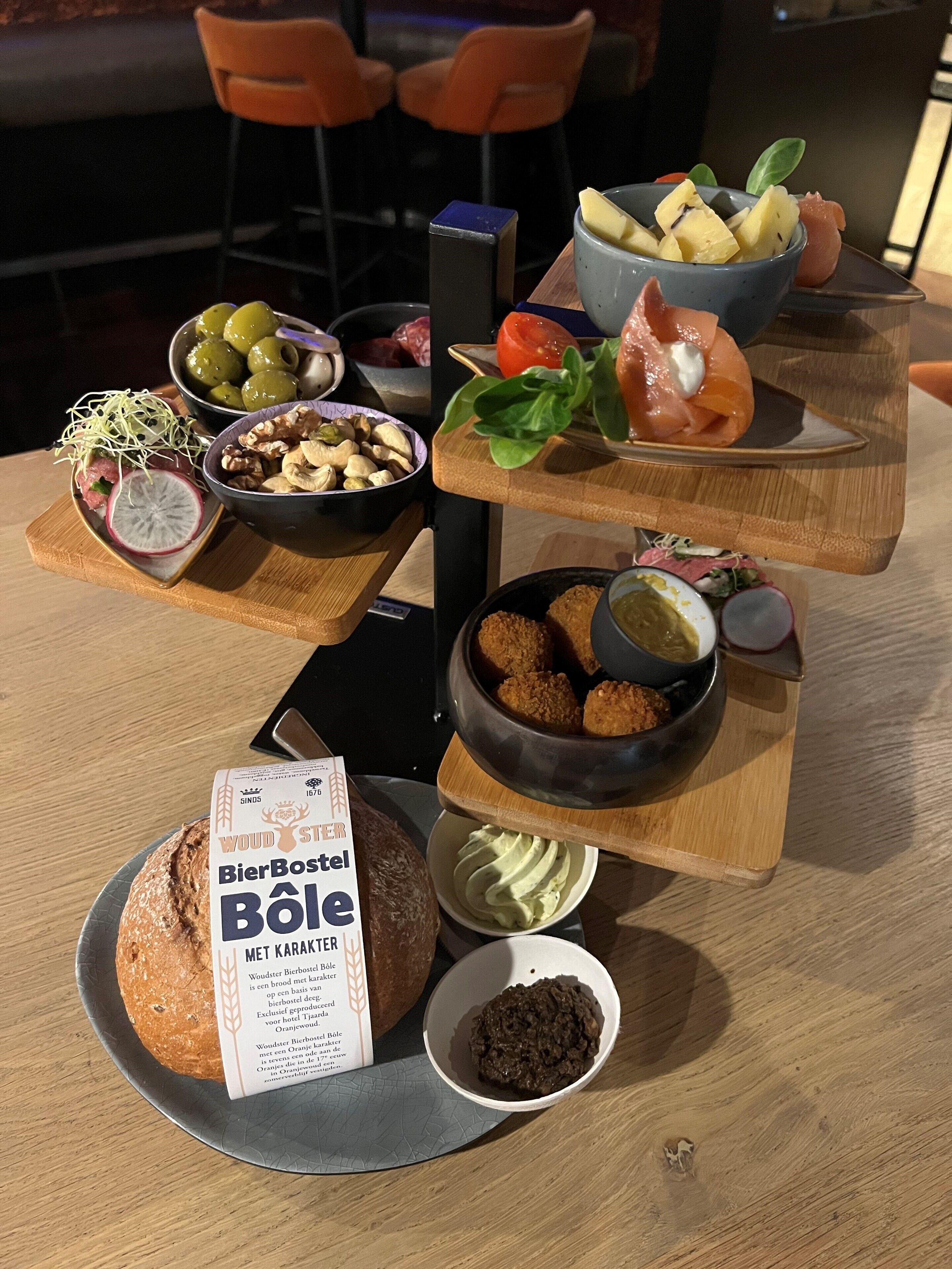 A wooden table with a variety of food items including bread, nuts, olives, and a bowl of what appears to be a salad.