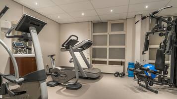 A gym with cardio machines, weightlifting equipment, and a window with blinds.
