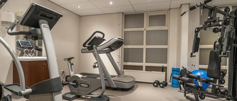 Un gimnasio con máquinas de cardio, equipo de levantamiento de pesas y una ventana con persianas.