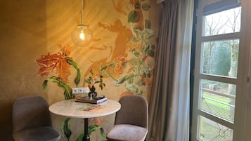 A room with a round table, two chairs, a floral mural, and a window with a view of greenery.