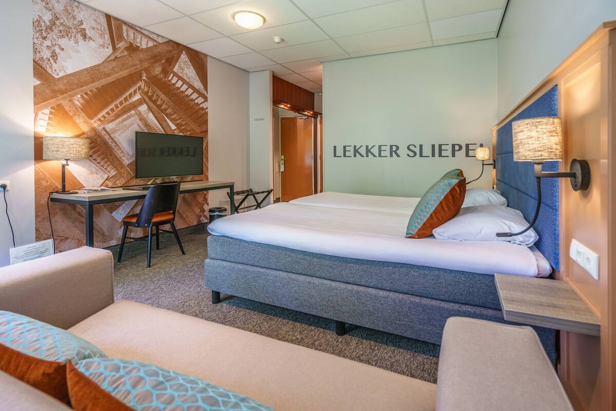 Une chambre d’hôtel comprenant un lit, un bureau avec un ordinateur, une chaise et un téléviseur fixé au mur.