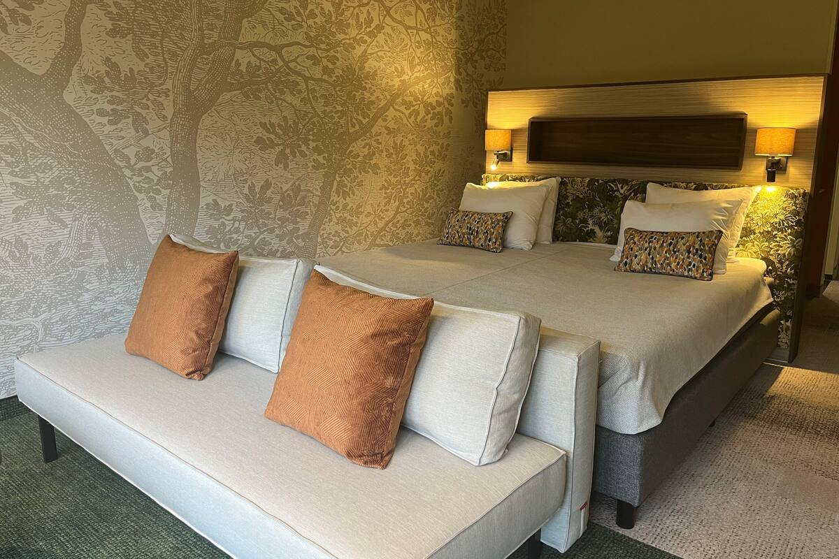 Une chambre d’hôtel avec un grand lit, deux tables de chevet avec des lampes, un canapé avec des coussins et un papier peint à motifs.