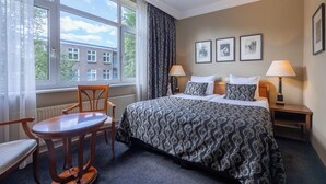 Een hotelkamer met een groot bed, twee nachtkastjes met lampen, een stoel en een raam met gordijnen.