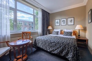 Une chambre d’hôtel avec un grand lit, deux tables de chevet avec des lampes, une chaise et une fenêtre avec des rideaux.
