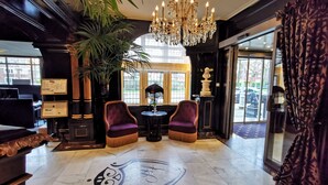 Un hall d’entrée luxueux, agrémenté d’un imposant lustre, de deux fauteuils confortables, d’une grande plante en pot et d’un sol en marbre orné d’un motif décoratif.