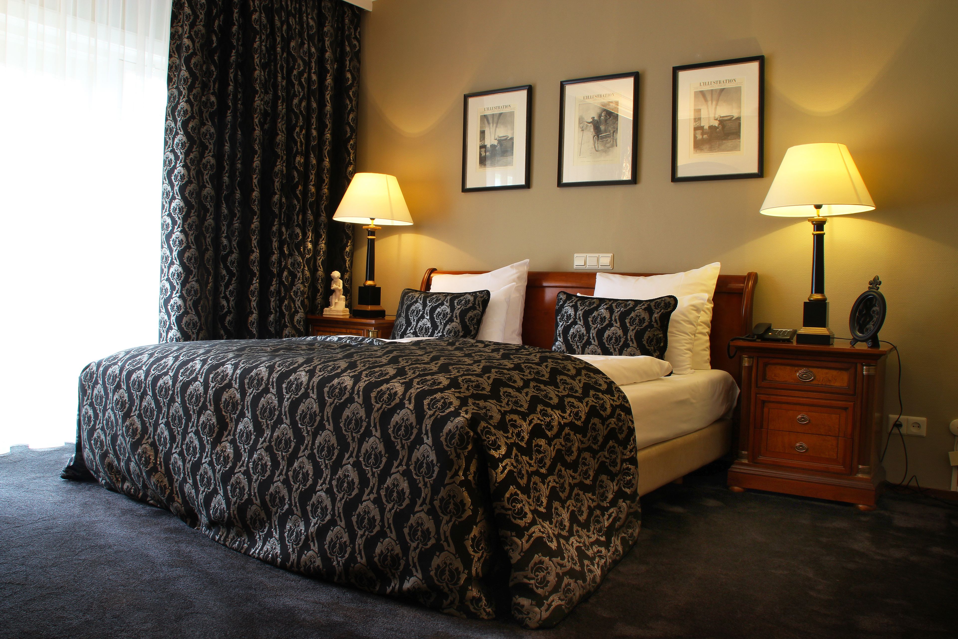 Een hotelkamer met een groot bed, twee nachtkastjes met lampen, een dressoir en drie ingelijste foto's aan de muur.