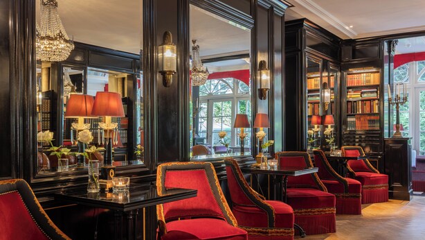 Een luxueuze kamer met een groot raam, elegante rode fauteuils en een goed gevulde boekenkast.