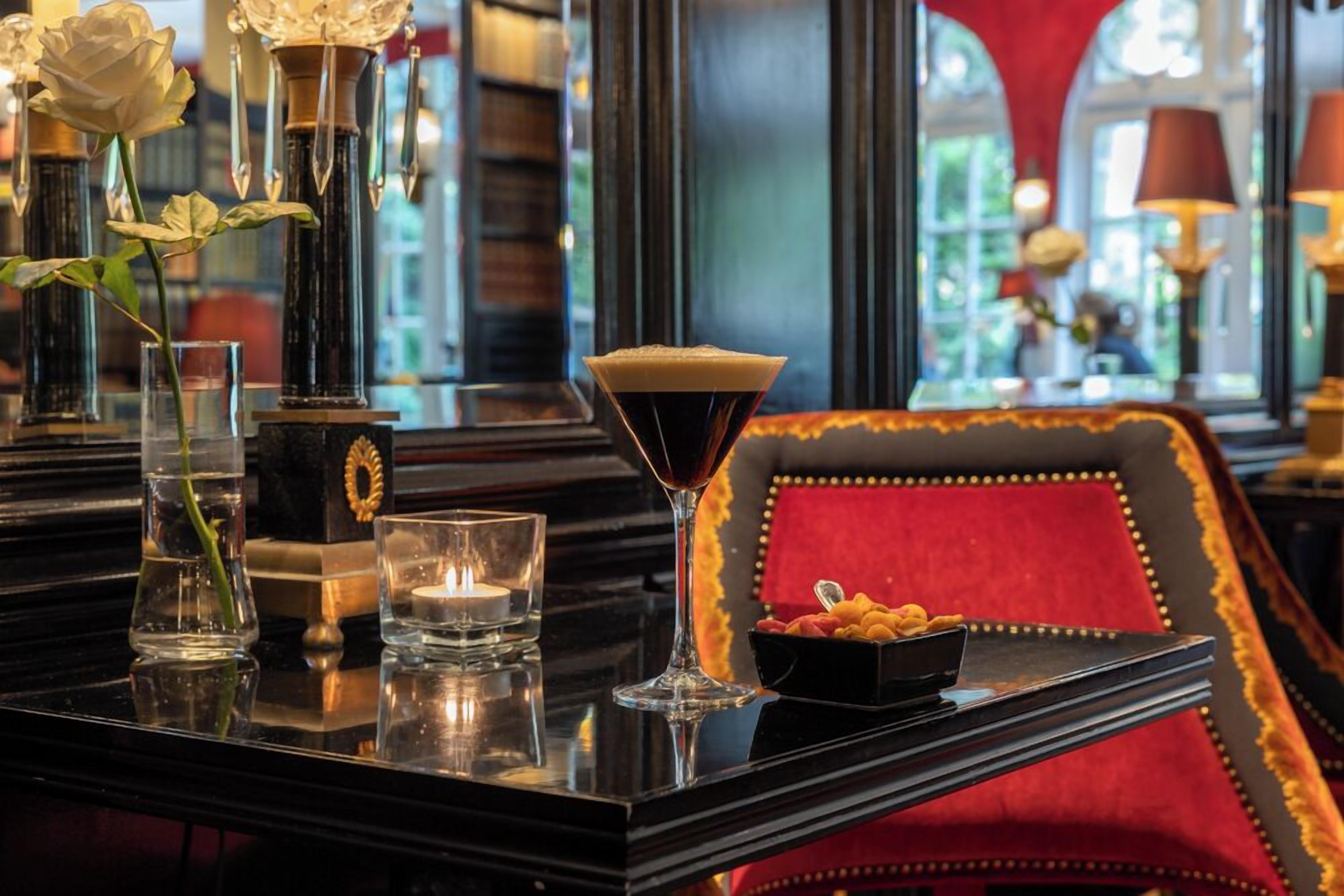 Un coin bar avec un verre à martini, un vase contenant une rose blanche et une bougie posée sur une surface réfléchissante.