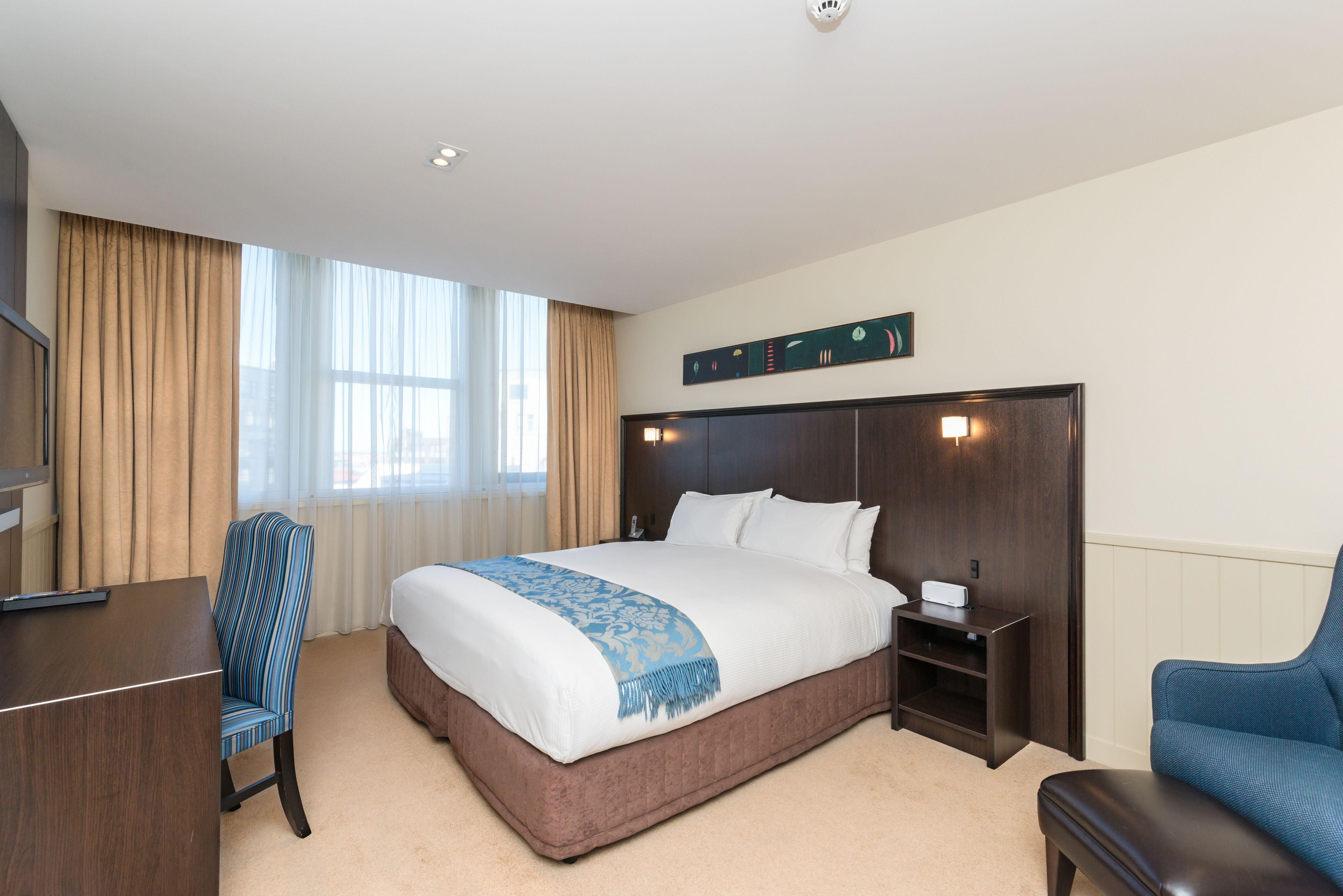 A hotel room with a large bed, a desk, a chair, and a nightstand.