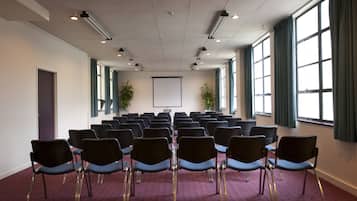 A conference room with rows of chairs, a projector screen, and large windows with curtains.