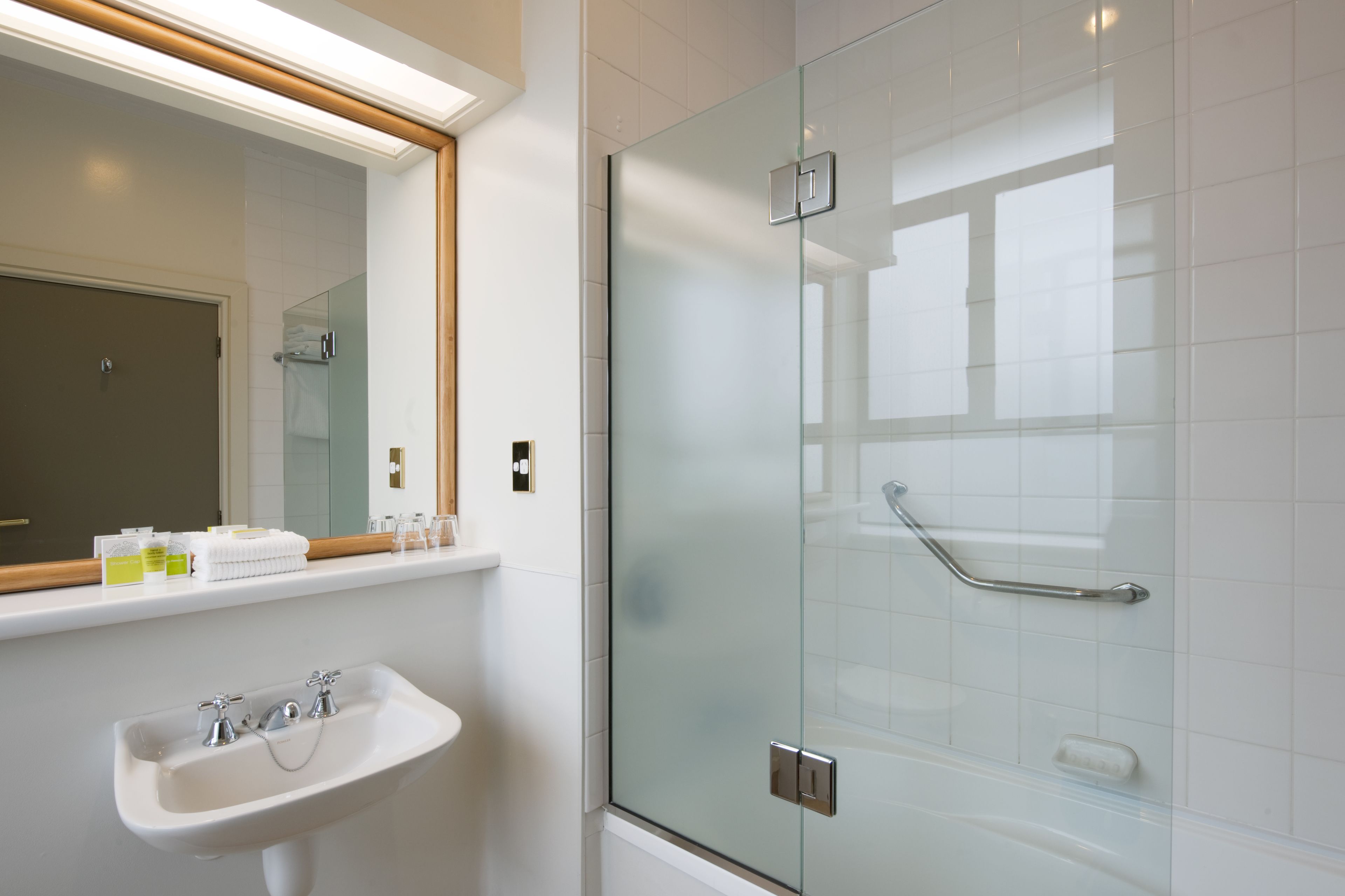 Een moderne badkamer met een douchecabine van glas, een witte wastafel en een spiegel boven de wastafel.