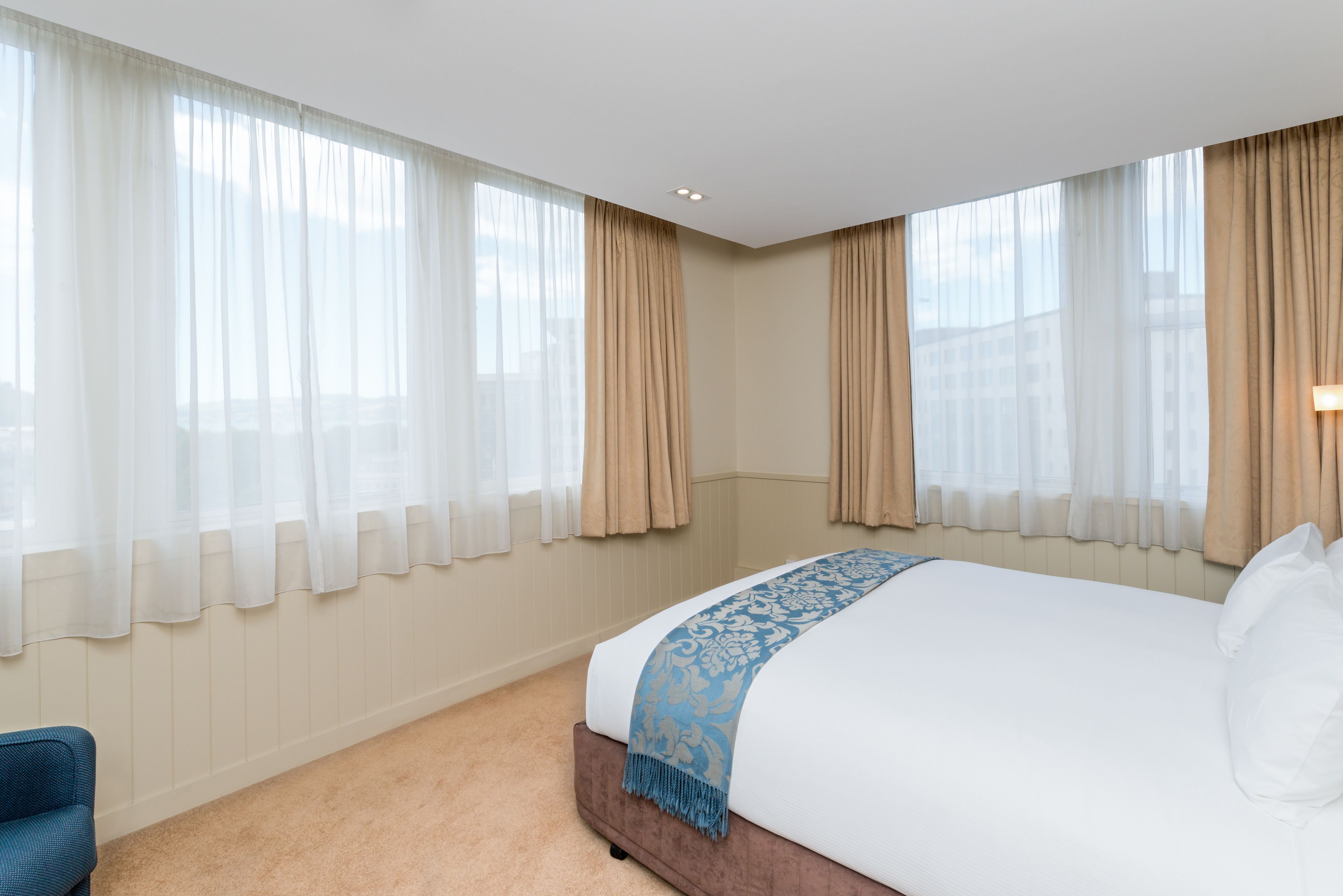 A hotel room with a large bed, beige walls, and curtains on the windows.