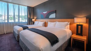 A hotel room with two beds, a large window with curtains, a painting on the wall, and a nightstand with a lamp. - Scenic Hotel Southern Cross (Dunedin)