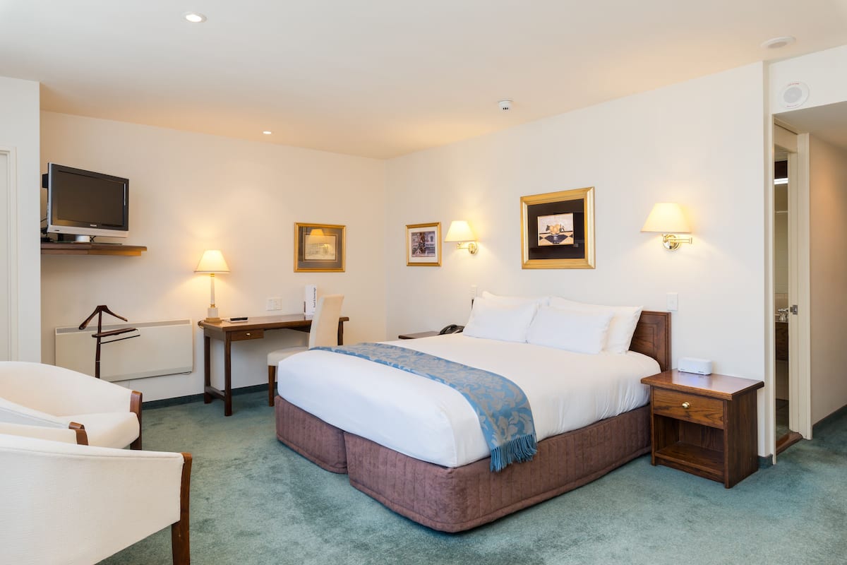 A hotel room with a large bed, a desk with a chair, a television, and two bedside lamps.