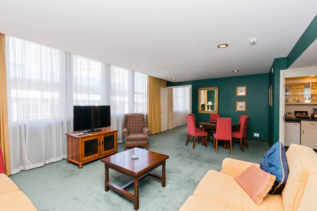 A living room with a sofa, coffee table, TV, and a dining area with chairs and a table.