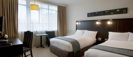 A hotel room with two beds, a desk, a chair, a lamp, and a window with curtains.