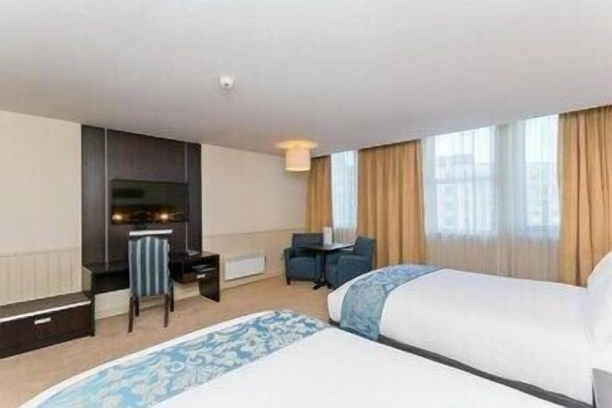 A hotel room with two beds, a desk, a chair, a TV, and a fireplace.