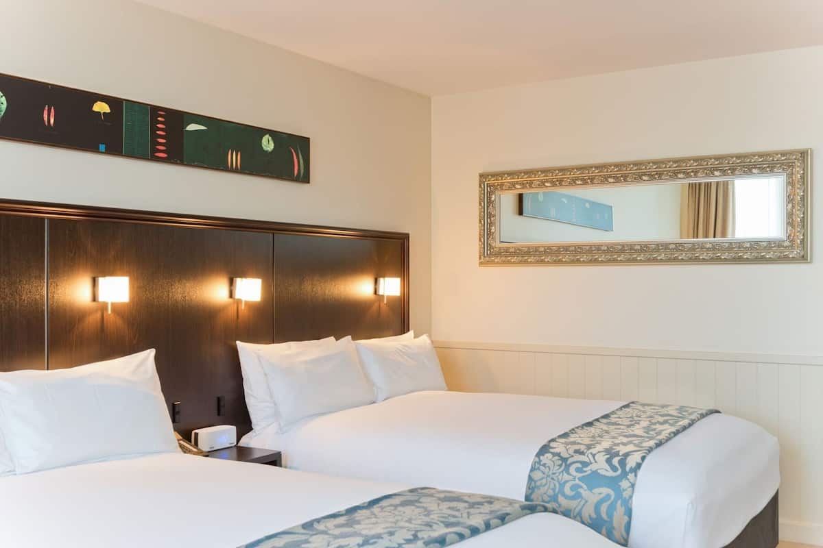 A hotel room with a large bed, two bedside tables, a wall-mounted mirror, and a decorative wall panel.