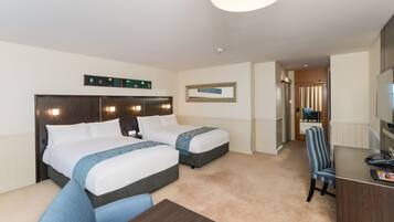 A hotel room with two beds, a desk, a chair, a TV, and a bathroom visible through an open door.