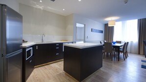A modern kitchen with a central island, a dining area with a table and chairs, and a view of the outdoors through large windows. - Scenic Hotel Southern Cross (Dunedin)