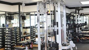 A gym with various exercise machines, weight racks, and a mirrored wall.