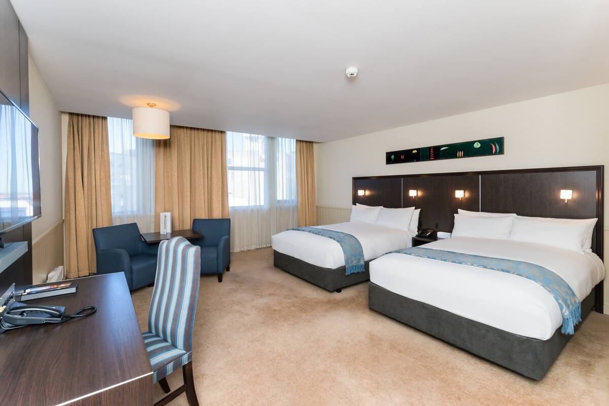 A hotel room with two beds, a desk, a chair, and a TV.