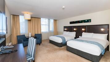 A hotel room with two beds, a desk, a chair, and a TV.