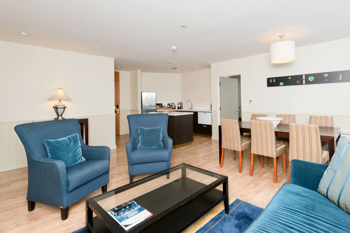 A modern living room with a sofa, two armchairs, a coffee table, and a dining area with chairs and a table.