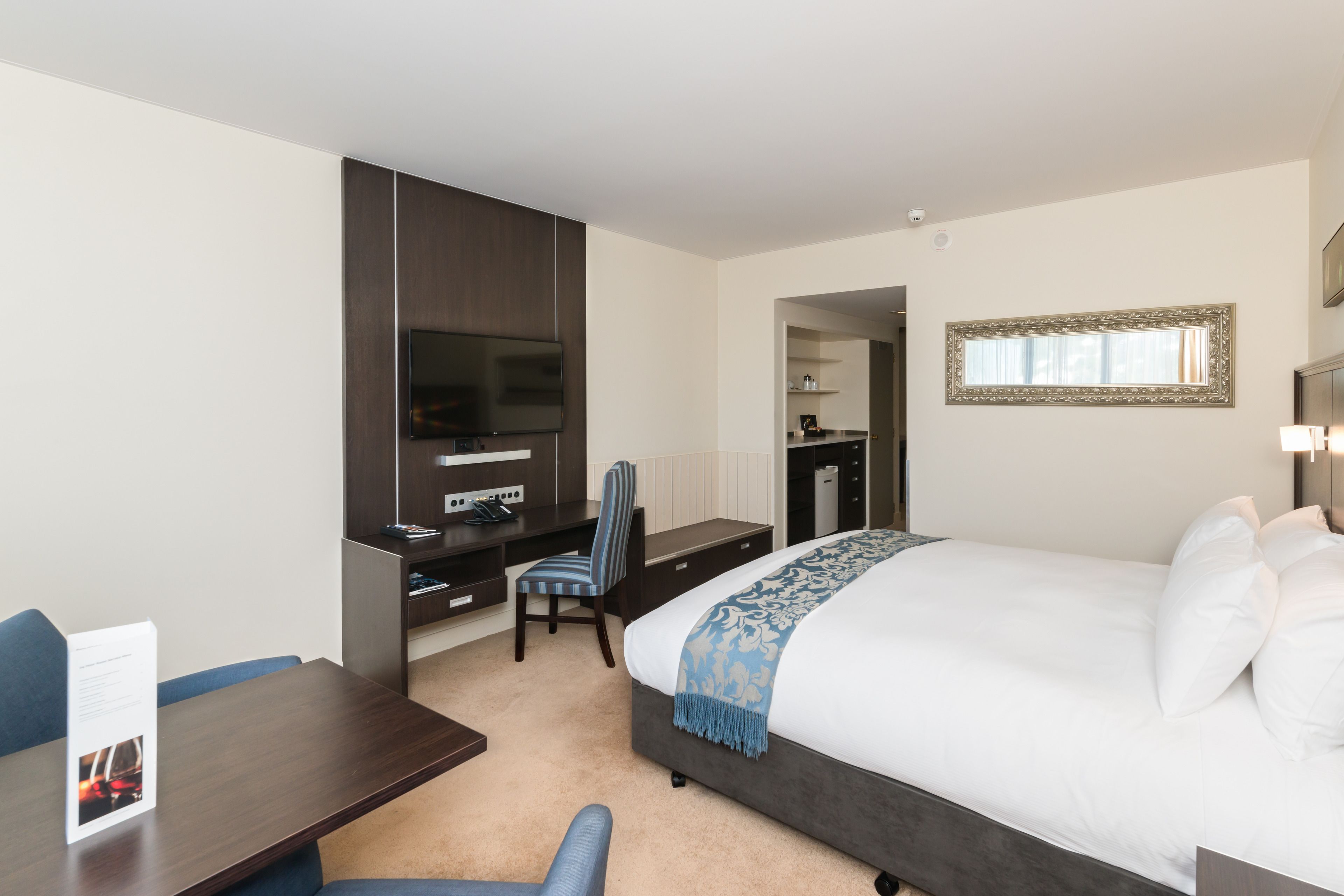 A hotel room with a bed, a desk, a chair, a TV, and a mirror.