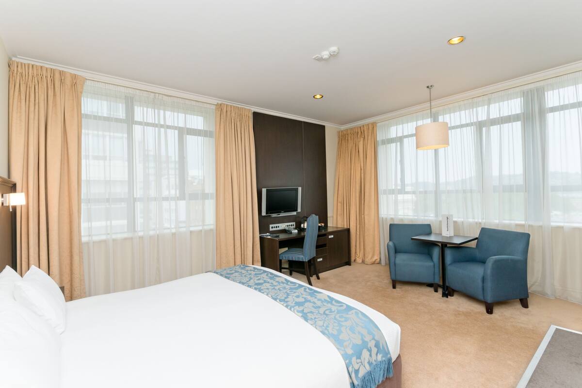 A hotel room with a large bed, a desk with a computer, two chairs, and a TV.