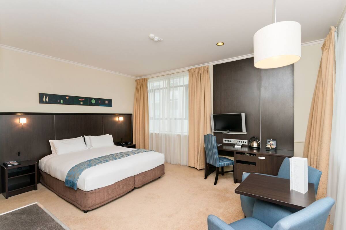 A hotel room with a bed, desk, chair, TV, and a wall-mounted artwork.