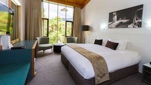 A hotel room with a large bed, a desk with a computer, a chair, a small table, and a large window with a view of greenery. - Scenic Hotel Franz Josef Glacier (Franz Josef Glacier)