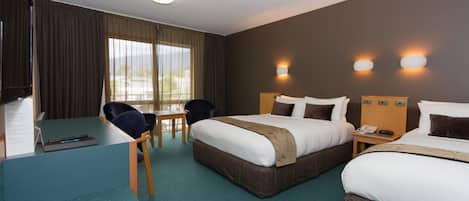 A hotel room with two beds, a desk, and a chair. There are two wall-mounted lamps and a window with curtains.