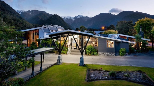 A modern house with a covered patio, a stone pathway, and a view of mountains. - Scenic Hotel Franz Josef Glacier (Franz Josef Glacier)
