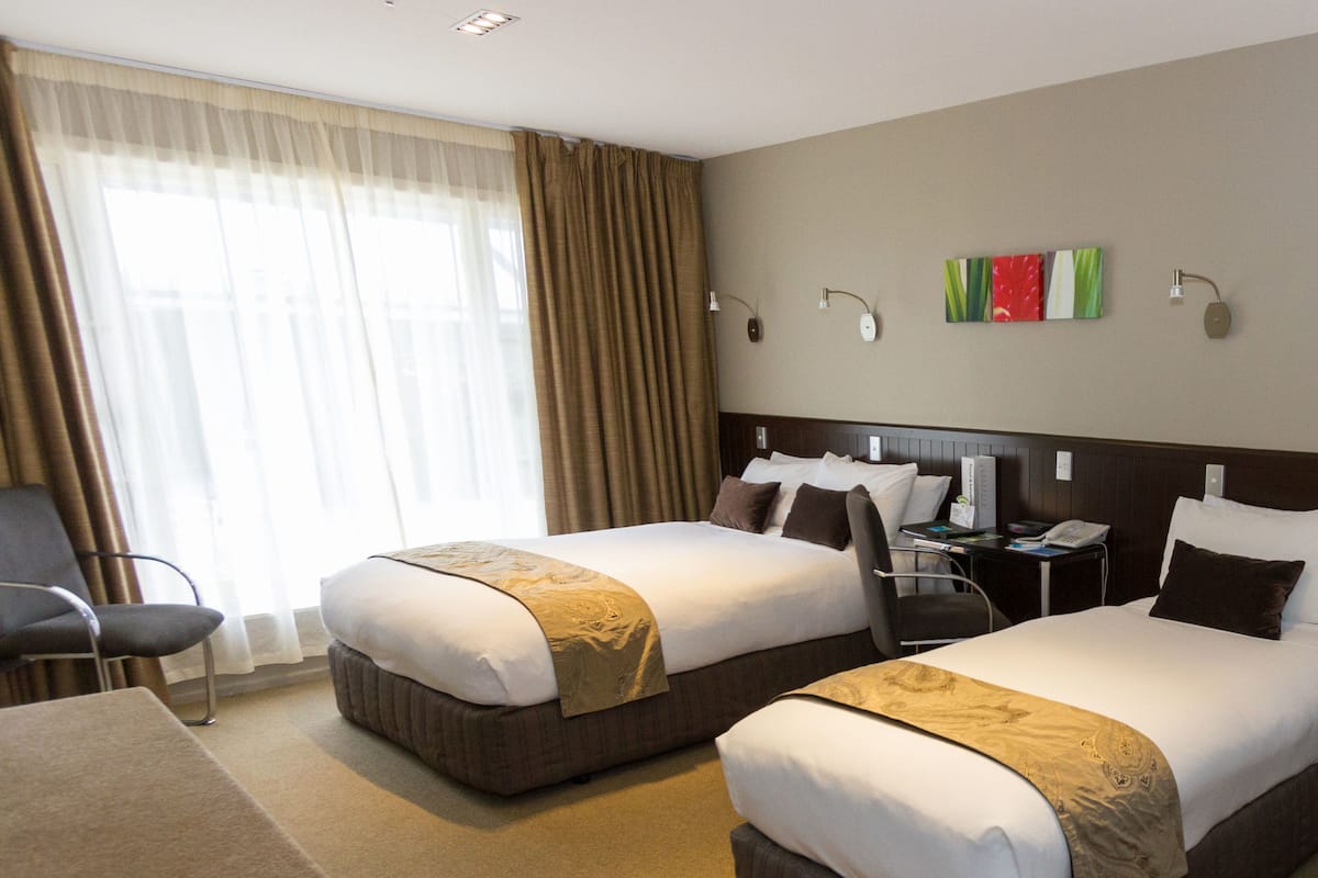 Una habitación de hotel con dos camas, un escritorio, una silla y un amplio ventanal con cortinas.