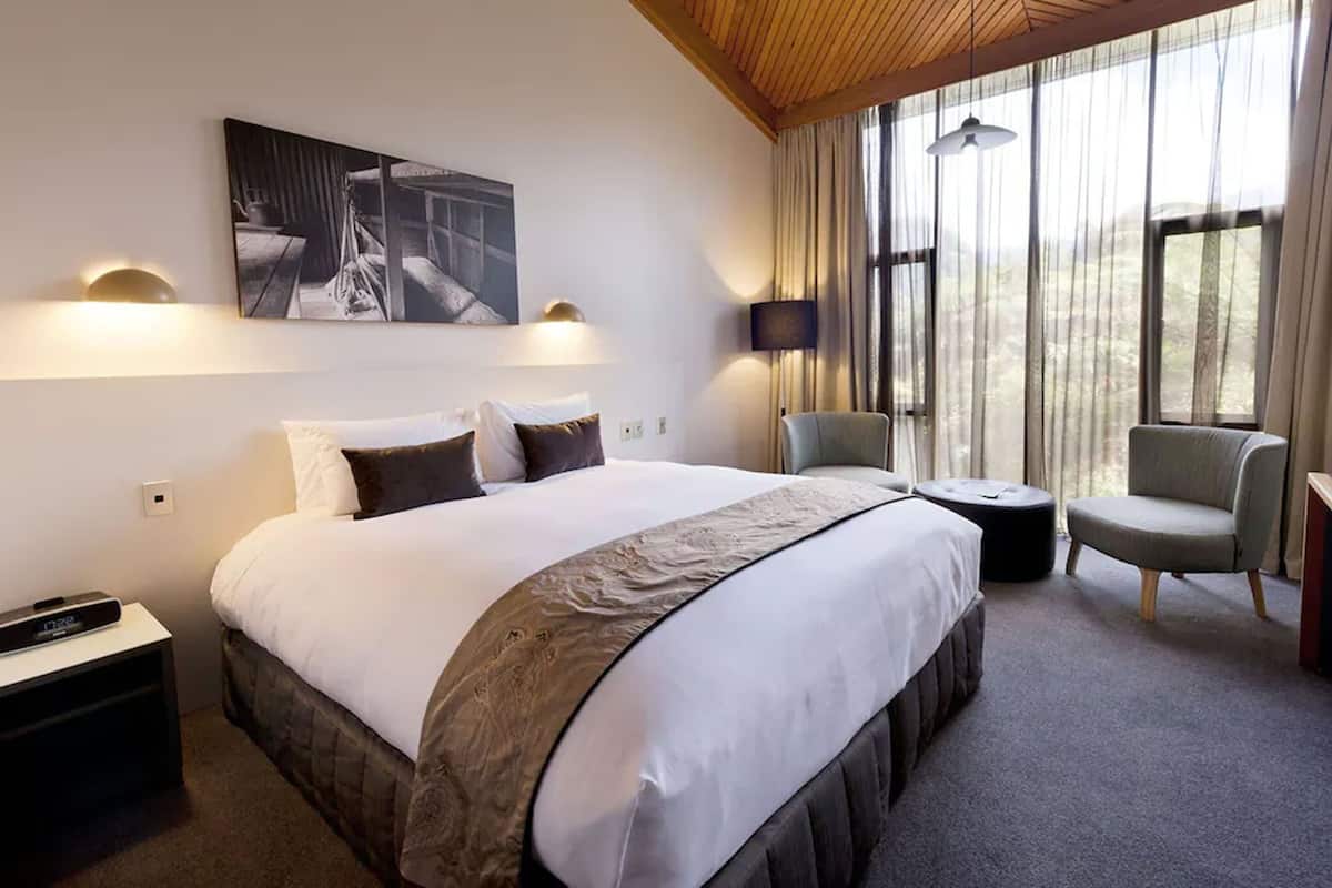 Una habitación de hotel con una cama grande, una silla, una mesita y un cuadro en la pared.