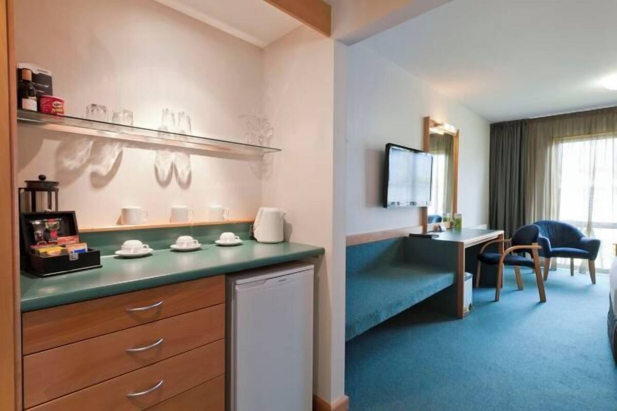 Habitación de hotel con kitchenette, escritorio, silla, televisión y ventana con cortinas.