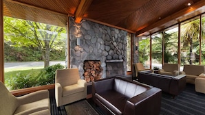 A modern lounge area with a stone fireplace, comfortable seating, and large windows offering a view of greenery. - Scenic Hotel Franz Josef Glacier (Franz Josef Glacier)