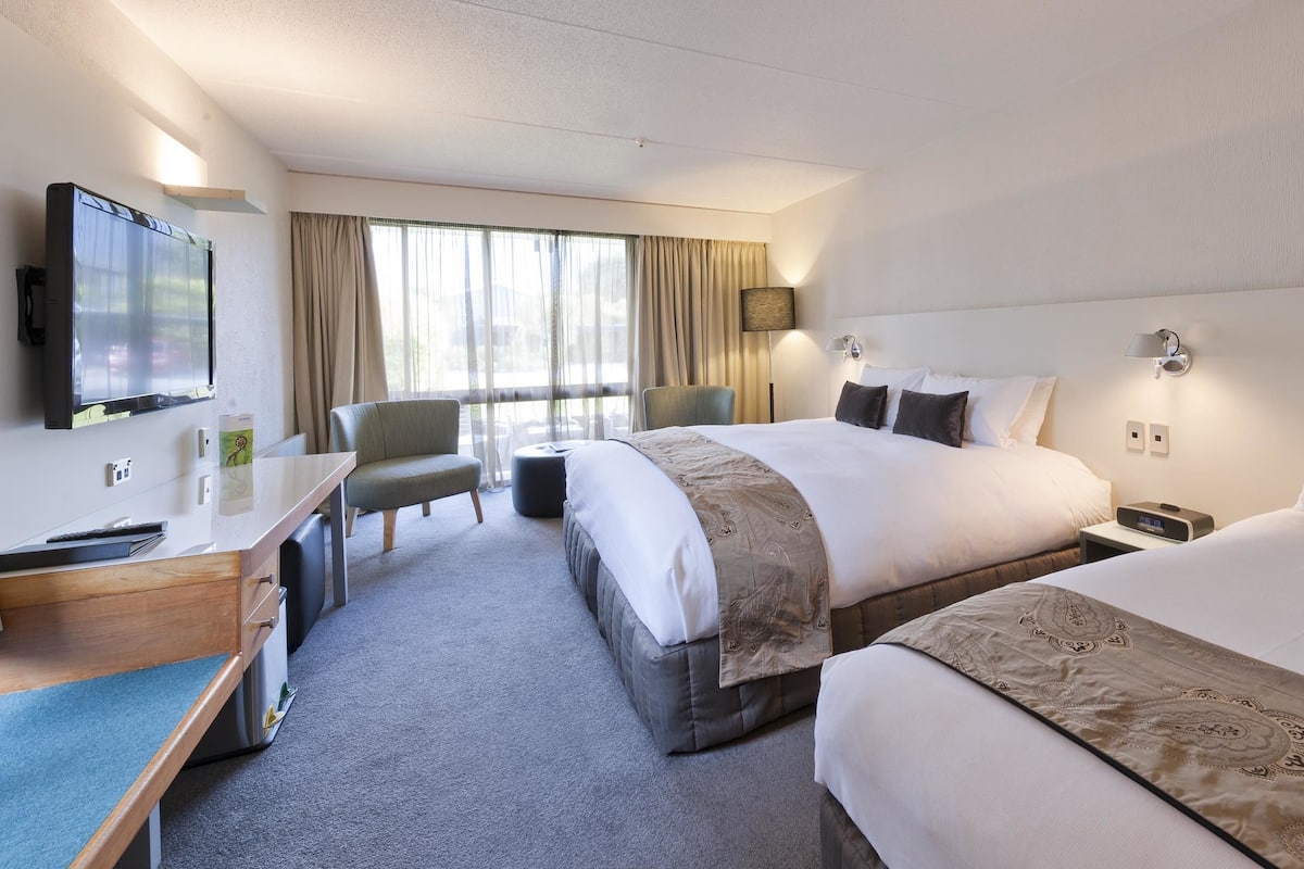 A hotel room with two beds, a desk, a chair, a TV, and a window with curtains.